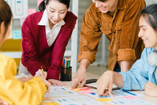 Hombres de negocios asiáticos y mujeres de negocios que se reúnen para intercambiar ideas sobre la aplicación de planificación de diseño web creativo y desarrollar el diseño de la plantilla para proyectos de teléfonos móviles que trabajan juntos en una oficina pequeña