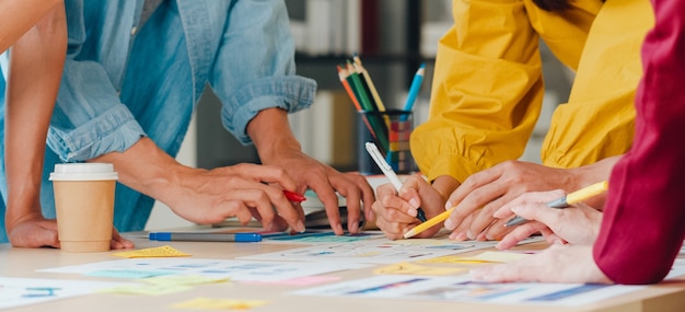 Hombres de negocios asiáticos y mujeres de negocios que se reúnen para intercambiar ideas sobre la aplicación de planificación de diseño web creativo y desarrollar el diseño de la plantilla para proyectos de teléfonos móviles que trabajan juntos en una oficina pequeña