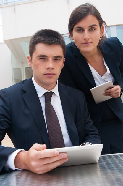 Hombres de negocios serios que presentan en la cámara y que sostienen las tabletas