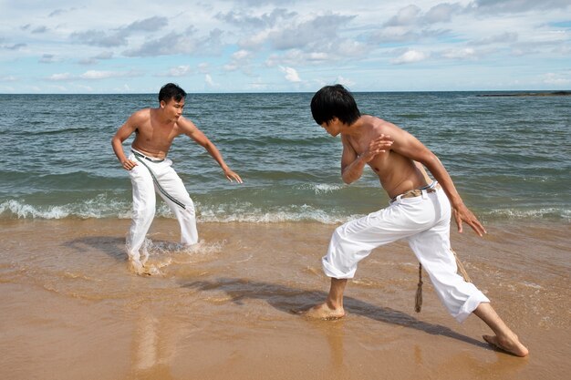 Hombres en la playa practicando capoeira juntos