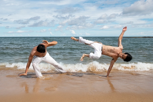 Hombres en la playa practicando capoeira juntos