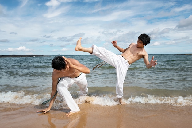 Foto gratuita hombres en la playa practicando capoeira juntos