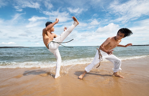 Hombres en la playa practicando capoeira juntos