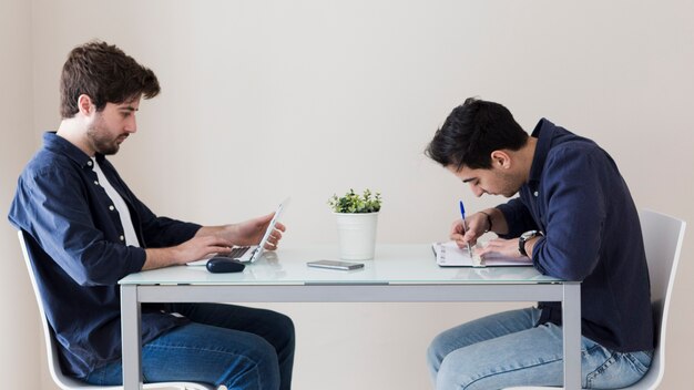 Hombres que usan la computadora portátil y haciendo notas