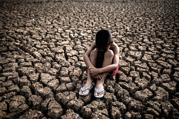 Hombres sentados abrazando sus rodillas, doblados, inclinados sobre el suelo seco, el calentamiento global