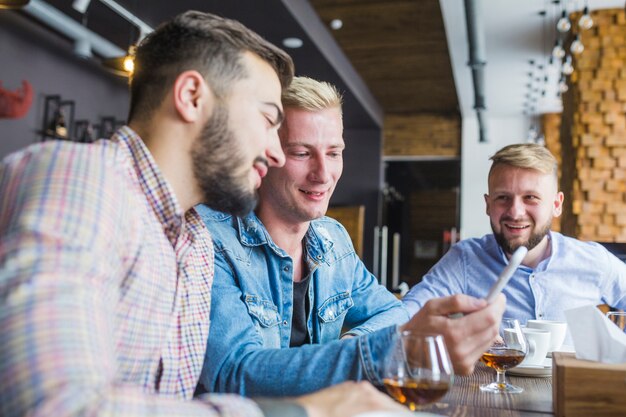 Hombres sentados en el restaurante mirando el teléfono móvil