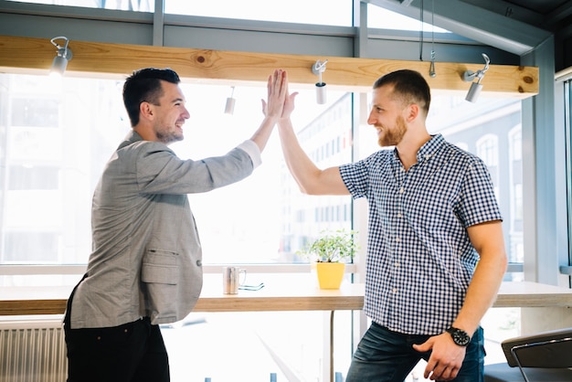 Foto gratuita hombres sonrientes dando hight-five en la oficina