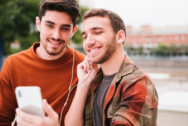 Hombres sonrientes escuchando música en el teléfono inteligente