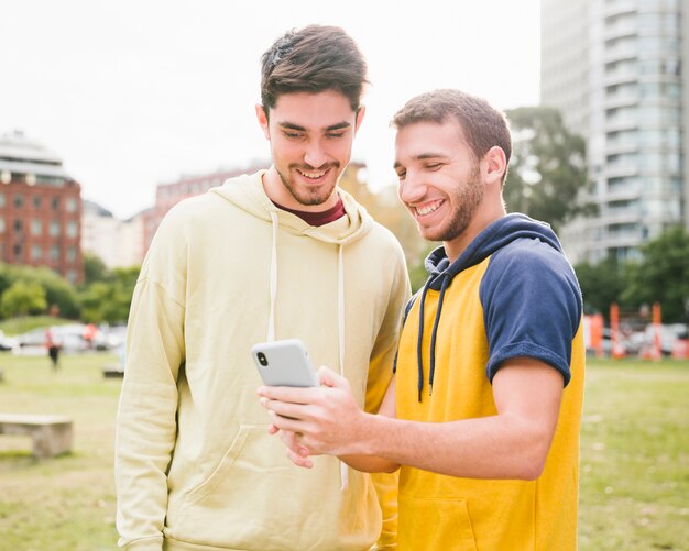 Hombres sonrientes que comparten smartphone en parque