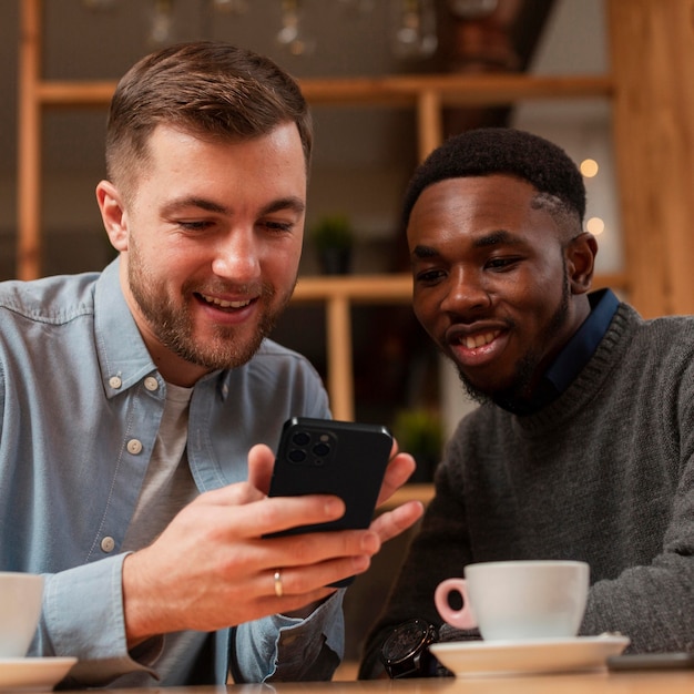 Hombres sonrientes con smartphone en un café