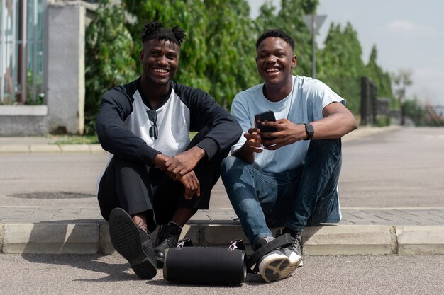 Hombres sonrientes de tiro completo sentados en la acera