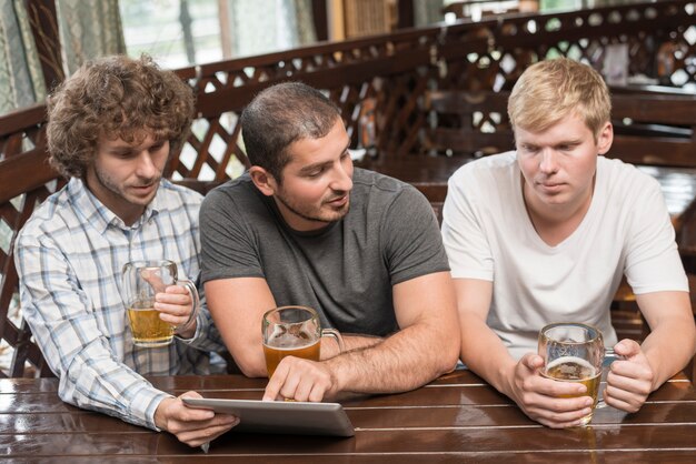 Hombres con tableta y cerveza hablando en pub