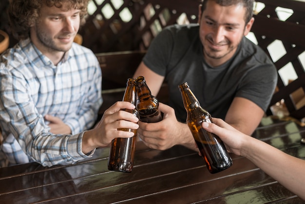 Hombres tintinean botellas con un amigo anónimo