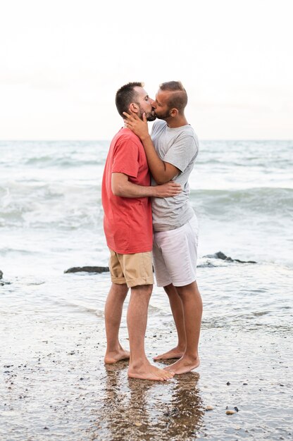 Hombres de tiro completo besándose en la orilla