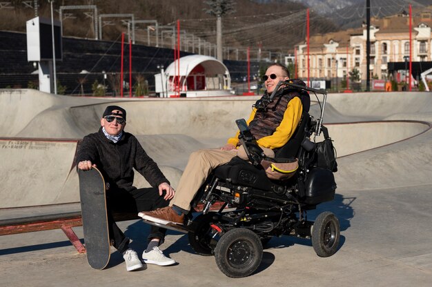 Hombres de tiro completo con silla de ruedas y patineta.