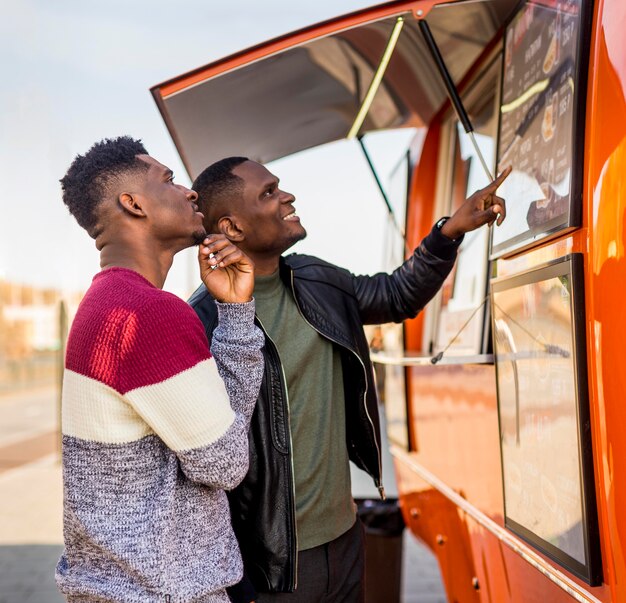 Hombres de tiro medio leyendo el menú del camión de comida