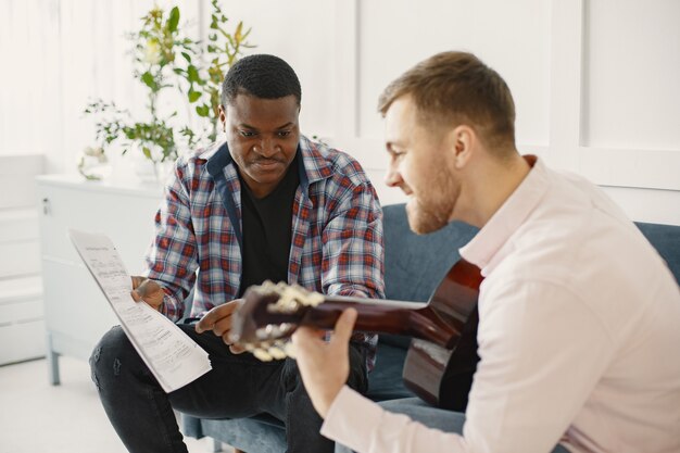 Los hombres tocan la guitarra. Escribiendo música. Hombres africanos y caucásicos.