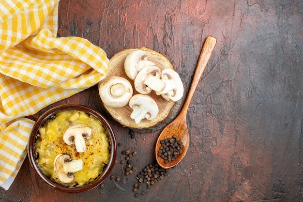 Hongo de vista superior con mosarella en tazón de pimienta negra en cuchara de madera setas en tablero de madera mantel amarillo sobre mesa rojo oscuro