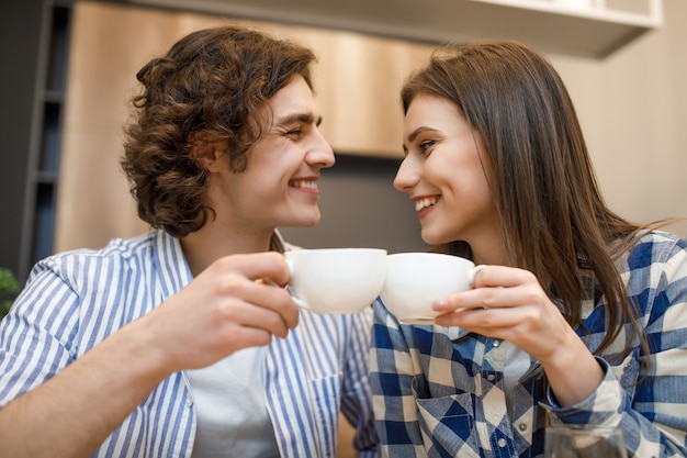 Hora del café en casa. Pareja joven romántica tomando café en la cocina de casa, sosteniendo la taza