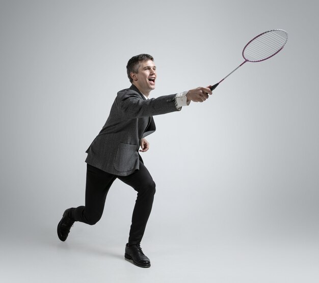 Hora de las emociones. Hombre en ropa de oficina jugando bádminton sobre fondo gris