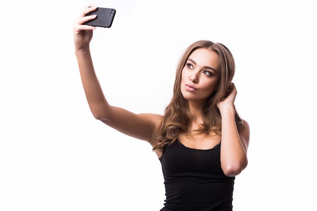 Hora de hacerse un selfie. Mujeres jóvenes alegres haciendo selfie por su teléfono inteligente en la pared gris