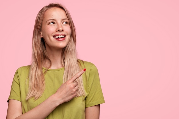 Horizontal retrato de alegre alegre mujer europea con suave sonrisa con dientes, apunta en la esquina superior derecha, nota algo fantástico