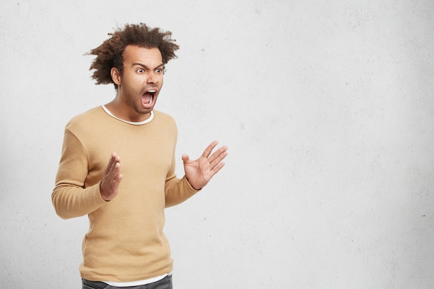 Horizontal retrato de furioso hombre de piel oscura tiene el pelo nítido, viste ropa casual,