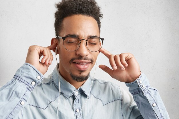 Horizontal retrato de hombre elegante de piel oscura con peinado afro, cierra los ojos en el disfrute,