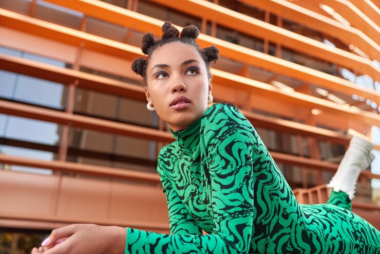 Photo Gratis horizontal shot of pretty young woman with hair buns applies blue eyeliner dressed in green costume and boots focused into distance during daytime considers something. people fashion style concept