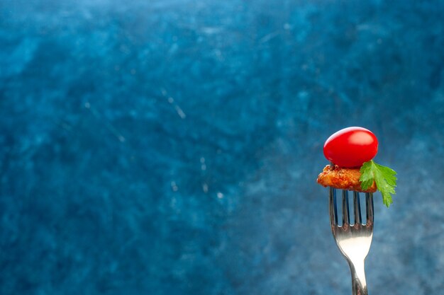 Horquilla con tomate y pollo sobre fondo azul.