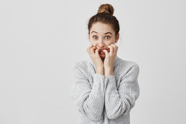 Horrorizada mujer con el pelo en el moño mirando asustada mordiéndose las uñas en tensión. Gerente de ventas femenino está en problemas para expresar emociones negativas. Concepto de terror y miedo