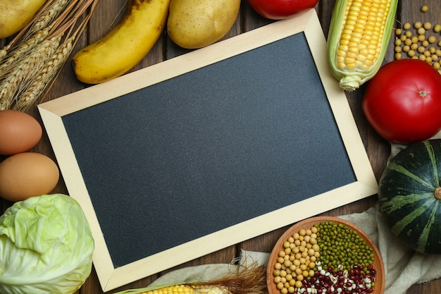 Hortalizas orgánicas frescas, frutas, huevos, frijoles y granos con pizarra en mesa de madera de época