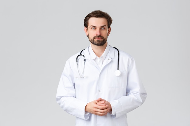 Hospital, trabajadores sanitarios, concepto de tratamiento covid-19. Joven médico en matorrales haciendo diligencias diarias en la clínica, escuchando los síntomas del paciente, mira la cámara, médico profesional curando enfermedades