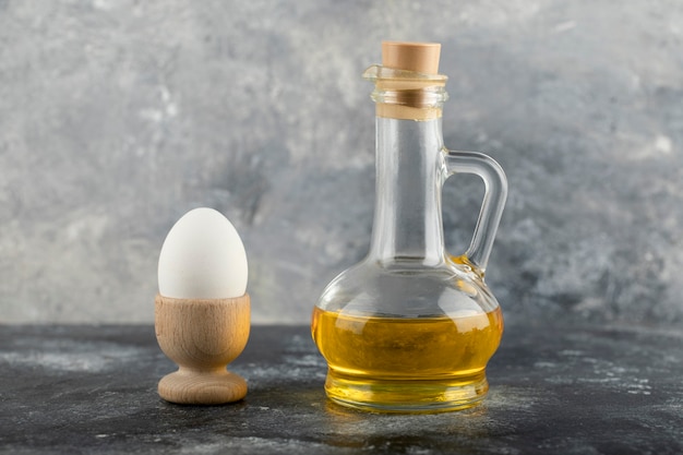 Una huevera de madera con huevo de gallina cocido y una botella de vidrio con aceite.