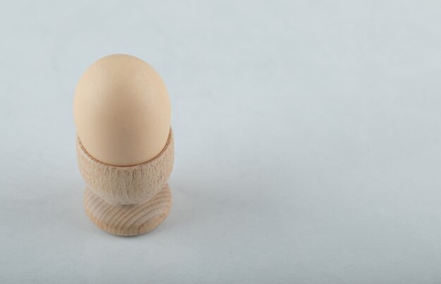 Huevo cocido en huevera de madera sobre fondo blanco.