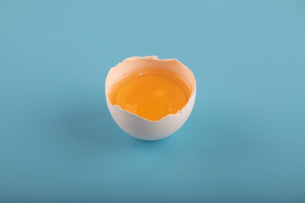 Huevo crudo roto sobre superficie azul.