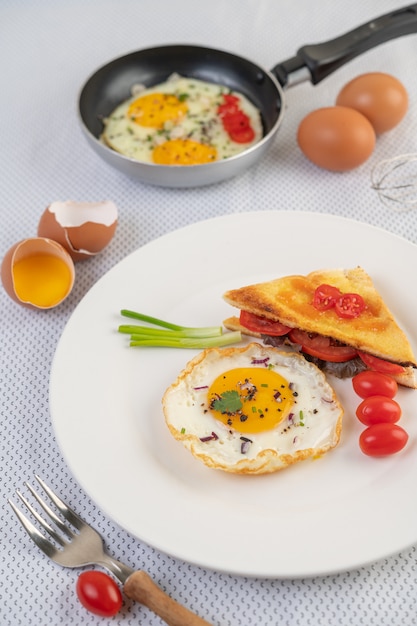 Huevo frito en un plato blanco con tostadas, rodajas de cebolla tierna y tomates en rodajas