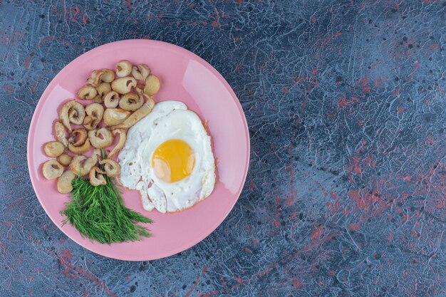 Huevo frito salado y condimentado con perejil en un plato rosa.