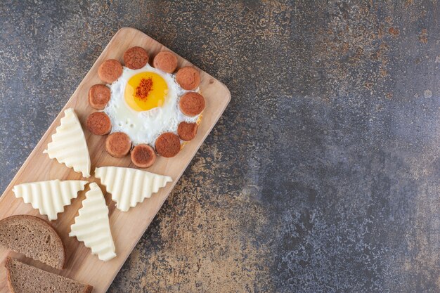 Huevo frito con salchichas y rodajas de queso en una bandeja de madera