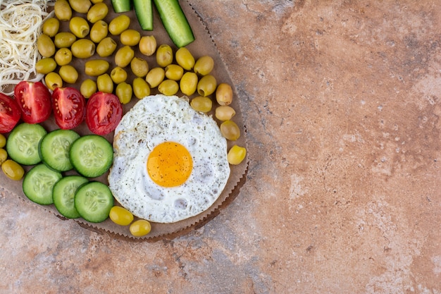 Huevo frito servido con verduras y aceitunas en bandeja de madera