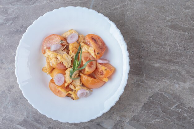 Huevo frito y tomates en un plato blanco.