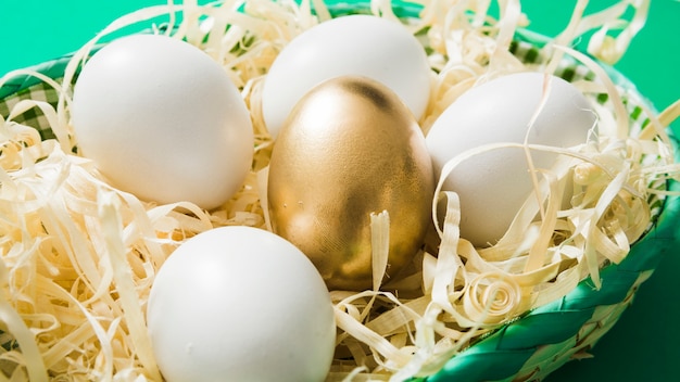 Un huevo de oro entre los huevos comunes en el afeitado de madera en el cuenco