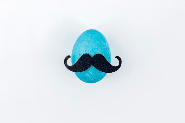 Foto gratuita huevo de pascua azul con bigote de papel en mesa