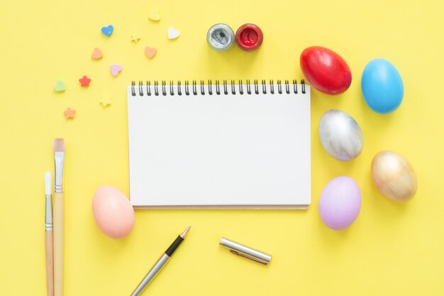 Huevo de Pascua colorido de la vista superior de la endecha plana pintado en la composición de los colores en colores pastel y mock up el cuaderno en blanco
