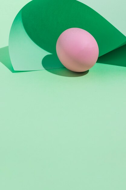 Huevo de Pascua rosado debajo de la hoja de papel enrollada en la tabla