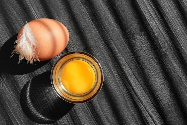 Huevo de pollo y yema con un vaso sobre una mesa de madera oscura con espacio para copiar luz solar sobre una mesa de madera y rayas de sombra