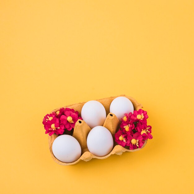 Huevos blancos en estante con flores en la mesa