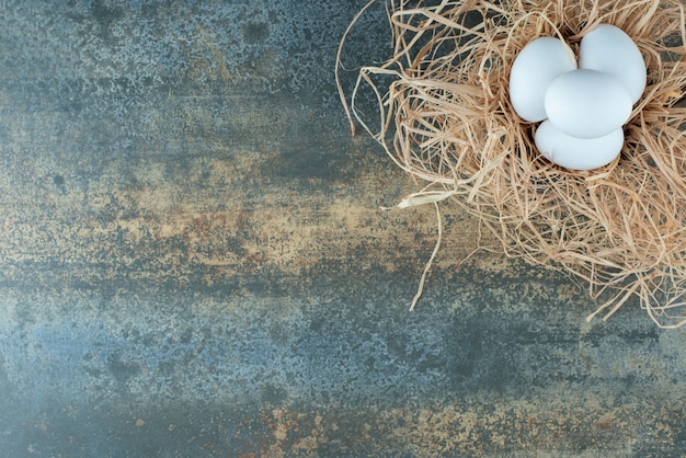 Huevos blancos frescos de pollo en heno sobre fondo de mármol