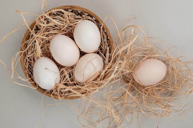 Huevos blancos de gallina fresca con heno en cesta de mimbre.