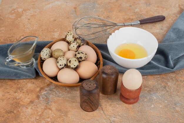 Huevos blancos y huevos de codorniz en la canasta con yema de huevo en la placa blanca.